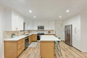 Kitchen with appliances with stainless steel finishes, light wood-type flooring, white cabinets, a kitchen island, and recessed lighting
