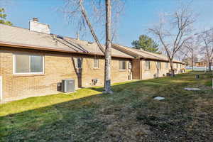 Back of house featuring a chimney, a yard, brick siding, and roof with shingles