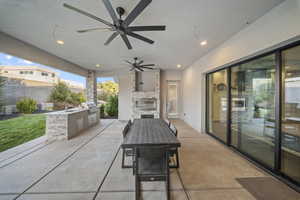 View of patio with an outdoor kitchen, a ceiling fan, outdoor dining area, and an outdoor stone fireplace