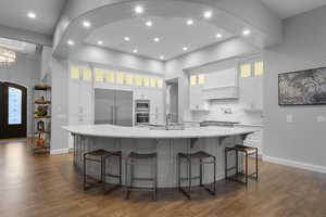 Kitchen featuring glass insert cabinets, a kitchen bar, built in appliances, light stone countertops, and white cabinets