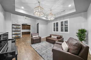 Living room with wood finished floors, a raised ceiling, recessed lighting, arched walkways, and a chandelier