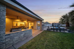 Patio terrace at dusk featuring a ceiling fan, a patio area, and exterior kitchen