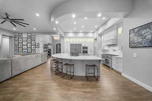 Kitchen with white cabinetry, a large island with sink, dark wood-type flooring, and recessed lighting