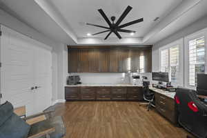 Office area featuring a raised ceiling, built in desk, dark wood-style floors, a ceiling fan, and recessed lighting