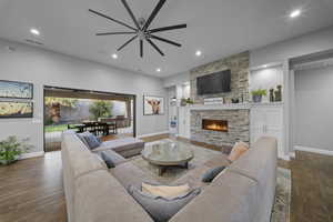 Living area with a stone fireplace, dark wood-type flooring, recessed lighting, and a ceiling fan
