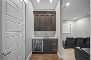 Indoor wet bar featuring dark brown cabinets, beverage cooler, recessed lighting, dark wood-type flooring, and light stone countertops