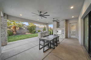 Fenced backyard featuring outdoor dining space, exterior kitchen, a patio, ceiling fan, and a fireplace