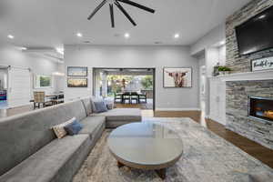 Living room with a barn door, a fireplace, wood finished floors, recessed lighting, and plenty of natural light