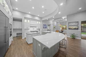 Kitchen featuring a breakfast bar, built in appliances, light stone counters, white cabinets, and dark wood finished floors