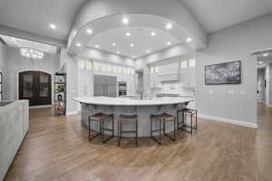 Kitchen featuring glass insert cabinets, a breakfast bar area, light wood-style floors, a large island with sink, and built in appliances