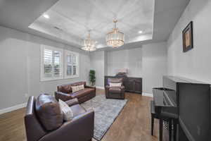Living room with a raised ceiling, dark wood finished floors, recessed lighting, and a chandelier