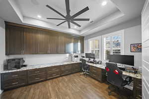 Office space with a raised ceiling, dark wood-style flooring, ceiling fan, and recessed lighting
