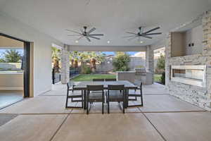 Fenced backyard featuring an outdoor kitchen, a patio, outdoor dining area, and an outdoor stone fireplace