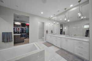 Bathroom with a walk in closet, double vanity, a bath, and recessed lighting