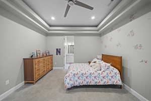 Bedroom featuring a ceiling fan, a tray ceiling, recessed lighting, ensuite bath, and light tile patterned floors