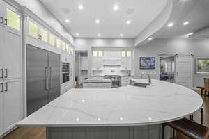 Kitchen with a barn door, light stone countertops, glass insert cabinets, recessed lighting, and built in appliances