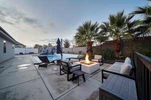 Patio terrace at dusk with a fenced backyard, an outdoor fire pit, and a patio area
