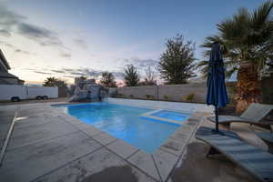 Pool at dusk featuring a fenced backyard, a patio area, and a pool with connected hot tub