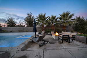Pool at dusk featuring a patio, a fenced backyard, a pool with connected hot tub, and an outdoor fire pit