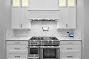 Kitchen with white cabinetry, range with two ovens, light stone counters, and glass insert cabinets