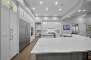 Kitchen featuring a barn door, light stone countertops, glass insert cabinets, dark wood finished floors, and white cabinetry