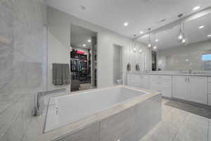 Bathroom with a walk in closet, vanity, a garden tub, and light marble finish floors