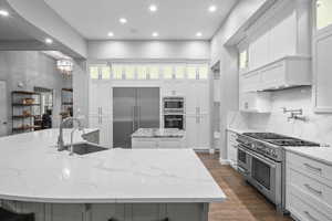 Kitchen featuring light stone counters, built in appliances, dark wood finished floors, glass insert cabinets, and recessed lighting
