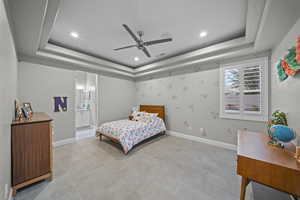 Bedroom featuring a ceiling fan, a tray ceiling, recessed lighting, and ensuite bathroom