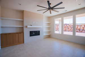 Unfurnished living room featuring built in features, a glass covered fireplace, and a ceiling fan