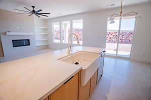 Kitchen with built in features, pendant lighting, light stone counters, a glass covered fireplace, and open floor plan