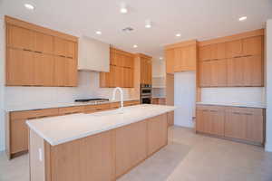 Kitchen featuring modern cabinets, light brown cabinets, recessed lighting, light stone countertops, and an island with sink