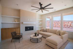 Living area with built in shelves, a glass covered fireplace, a ceiling fan, light tile patterned flooring, and recessed lighting