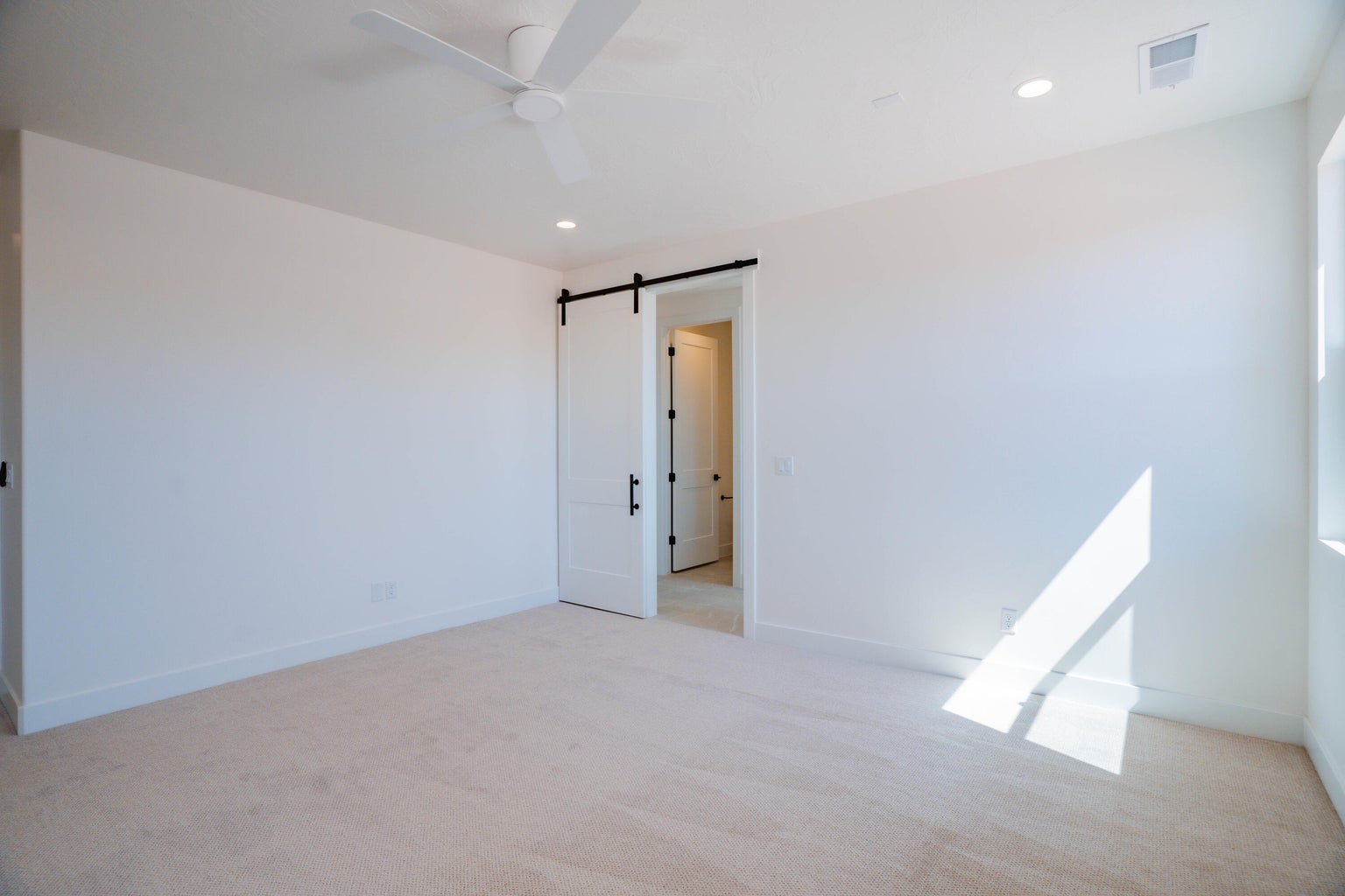 Empty room with a barn door, light colored carpet, recessed lighting, and ceiling fan