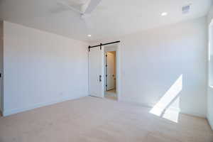 Empty room with a barn door, light colored carpet, recessed lighting, and ceiling fan