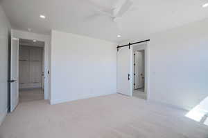 Unfurnished bedroom featuring a barn door, light carpet, recessed lighting, and a ceiling fan