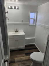 Bathroom featuring a textured wall, a wainscoted wall, vanity, dark wood finished floors, and a textured ceiling