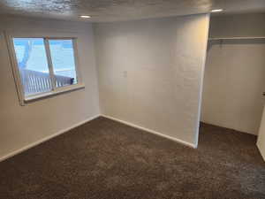 Unfurnished bedroom with a textured ceiling, a textured wall, dark colored carpet, and a closet