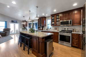 Kitchen featuring stainless steel appliances, hanging light fixtures, glass insert cabinets, a breakfast bar, and light wood-type flooring