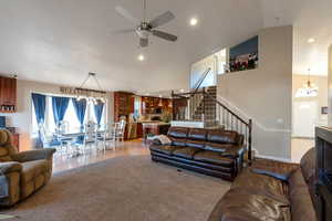 Living area with a chandelier, stairway, high vaulted ceiling, a ceiling fan, and light wood-style flooring
