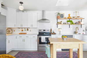 Kitchen with appliances with stainless steel finishes, wall chimney exhaust hood, backsplash, and white cabinets