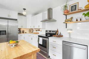 Kitchen featuring appliances with stainless steel finishes, wall chimney range hood, white cabinets, and open shelves