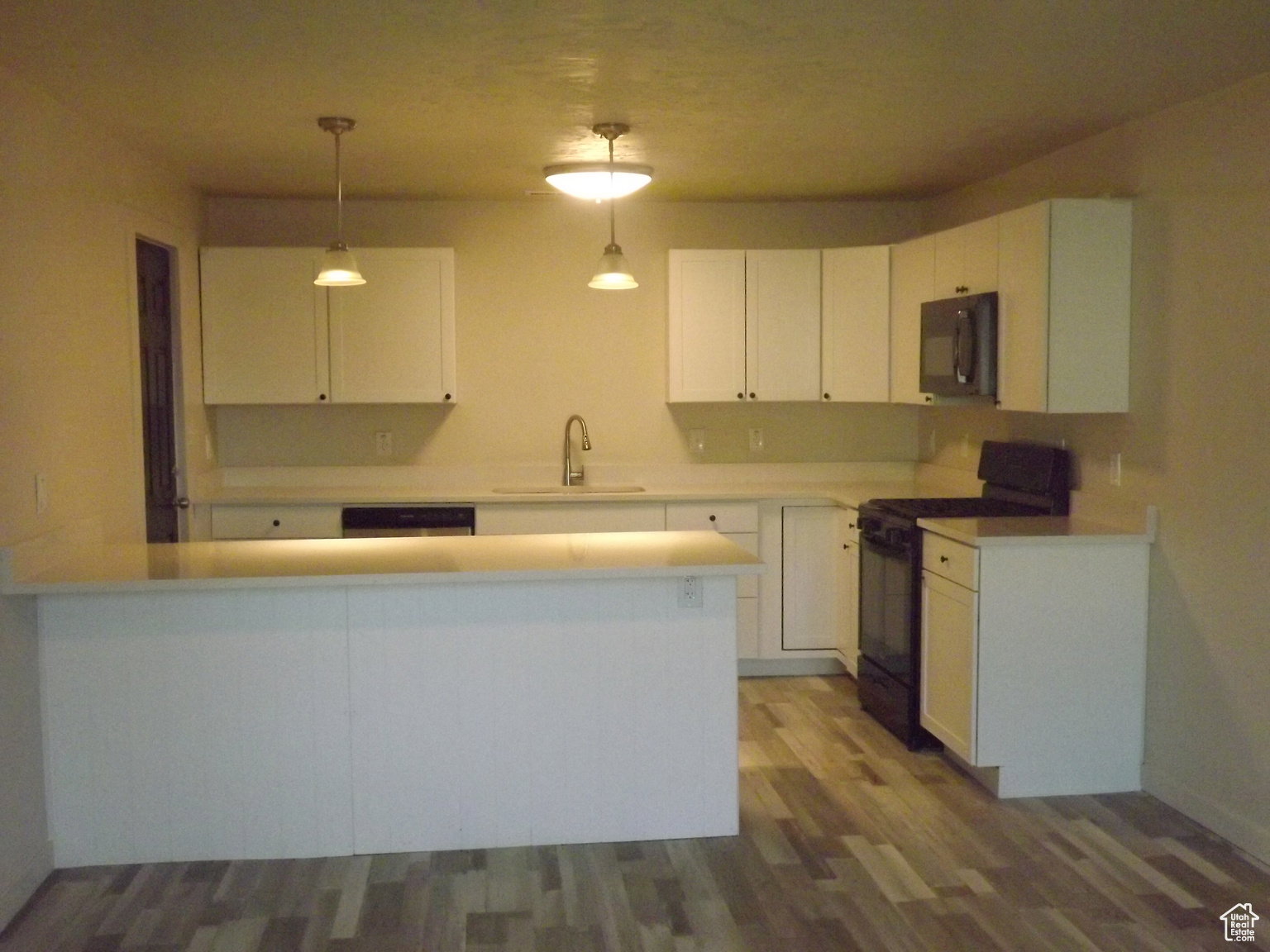 Kitchen with stainless steel appliances, hanging light fixtures, white cabinets, and  wood-type flooring