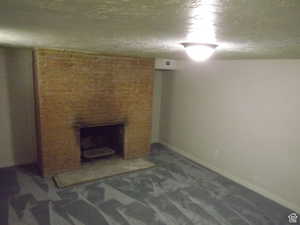 Finished basement with a brick fireplace, carpet flooring, and a textured ceiling