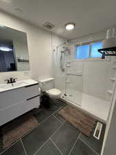 Bathroom with walk in shower, vanity, and dark tile patterned flooring