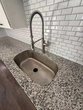 Kitchen view of light stone counters, white cabinets, and backsplash
