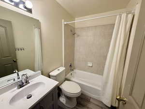 Bathroom featuring vanity, shower / bath combo, a textured ceiling, and wood finish floors