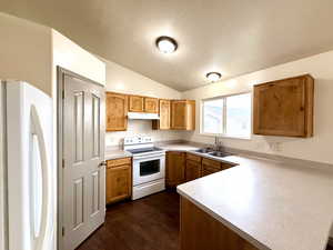 Kitchen featuring white appliances, light countertops, a textured ceiling, vaulted ceiling, and under cabinet range hood