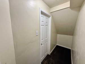 Interior space featuring a textured wall, a textured ceiling, dark carpet, and vaulted ceiling