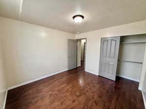 Unfurnished bedroom featuring a textured ceiling, dark wood-style flooring, and a closet