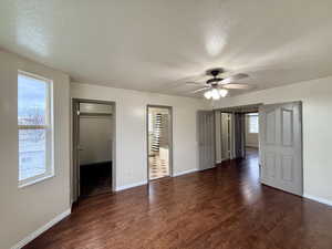 Unfurnished bedroom with a textured ceiling, a walk in closet, dark wood finished floors, and ceiling fan